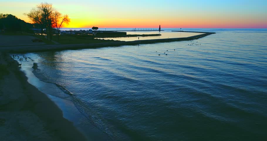Scenic flyby of Lake Michigan harbor with lighthouse at sunrise.
