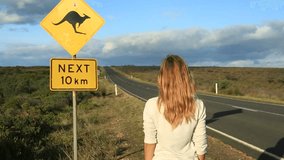 Joyful woman stands arms outstretched near kangaroo crossing sign
Cheering young woman arms outstretched on the road standing next to a kangaroo warning sign, Australia.