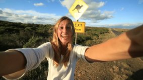 Young woman traveling takes selfie with kangaroo crossing sign
Cheering young woman takes a selfie portrait on the road standing next to a kangaroo warning sign, Australia.