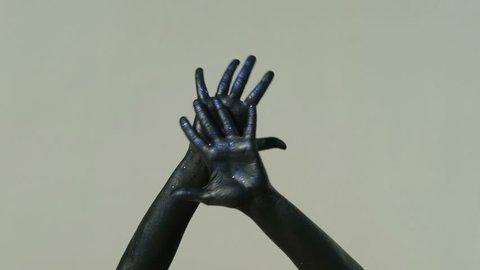 closeup shot of hands covered with black paint bright blue sequins move slowly in dance on gray background. Isolated arms on elbow in frame touch smoothly each other, fingering, showing flexibility of