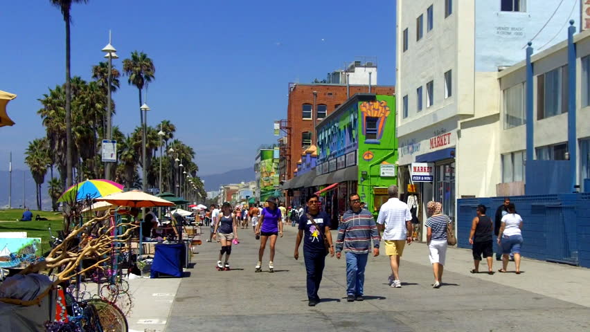 VENICE BEACH, CA - August 2, 2012:  Tourists walk and roller skate past merchant