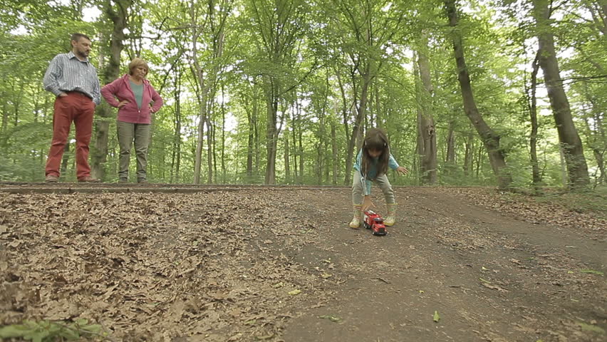 Little girl launching fire engine on dirt road in forest. Father and grand mother supervising.