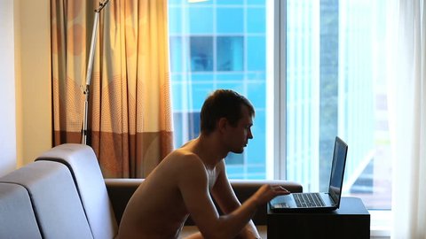 Man typing on laptop sitting on couch in front of big window