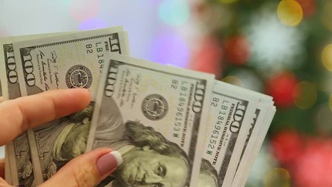 Closeup of female hands holding stack of money in blurry glowing holiday background. Adult woman counting money ready to buy Christmas presents. Real time full hd video footage