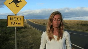 Cheering young woman takes a selfie portrait on the road standing next to a kangaroo warning sign, Australia.