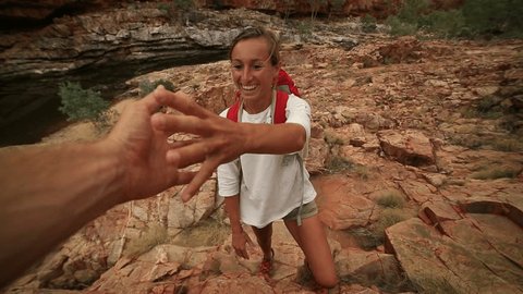 Caucasian female climbing the red rocks in the Australia's outback, pulls out her hand to get assistance from teammate. 