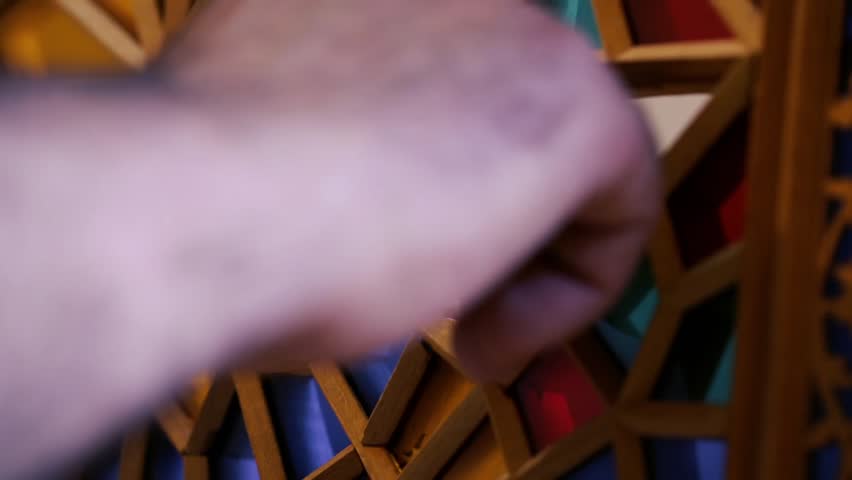 The master of stained glass puts pieces of cropped multicolored glass into wooden frames creating a composition. Azerbaijan old art.