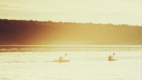 Two kayakers glide wide river on a background sunset