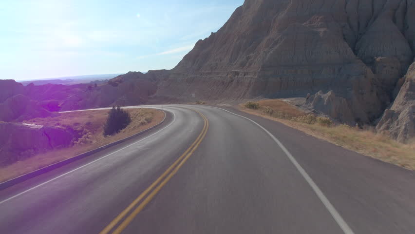 FPV: Driving along the empty road winding through beautiful Badlands landscape with rocky sandstone formations. Traveling across the Badlands desert in South Dakota. Road trip across United States.