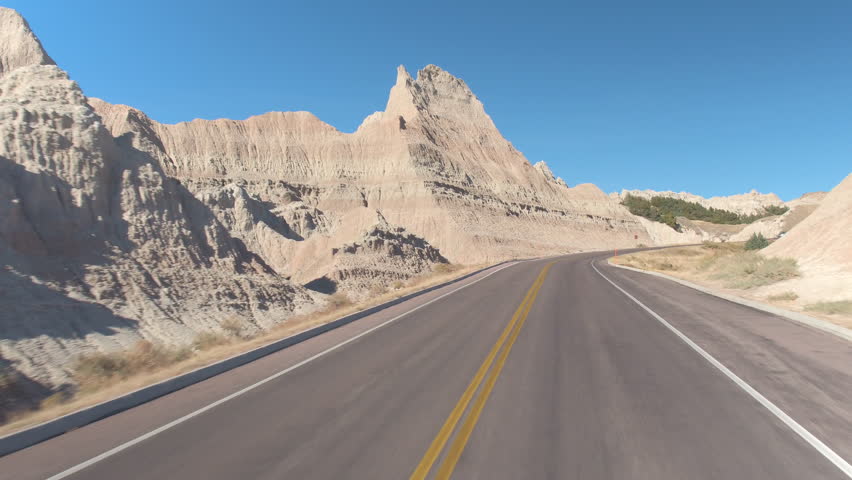 FPV: Driving along the empty road winding through stunning Badlands landscape with rocky sandstone formations. Traveling across the Badlands desert in South Dakota. Road trip across United States.