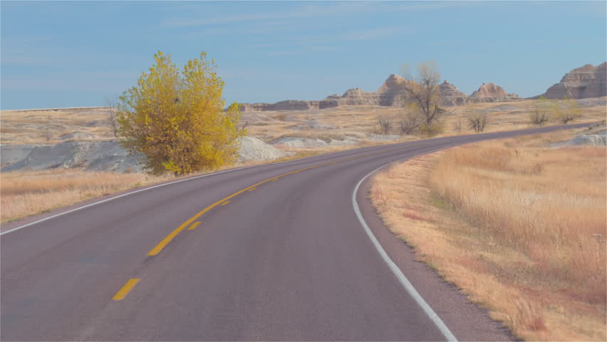 FPV: Driving along the empty road towards the picturesque Badlands landscape with rocky sandstone formations. Traveling across the Badlands desert in South Dakota. Road trip across United States.