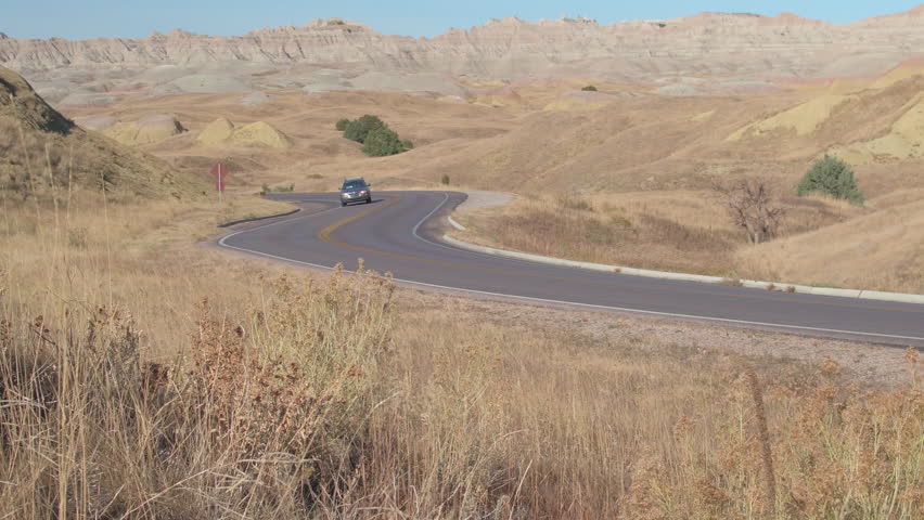Car driving along the road snaking through Badlands landscape past the rocky sandstone formations. People on road trip across the States driving on winding road through Badlands desert and mountains.