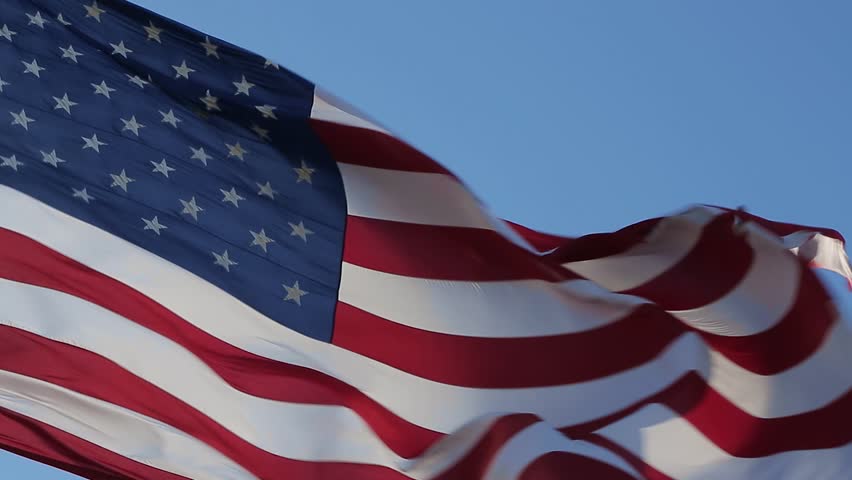 American flag is flying in the wind on a sunny day. Symbol of the Amenrican national holiday. Shooting close-up. Independence Day - American concept. Waving United states of America famous flag.