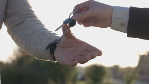 Hand of businessman giving keys to client. Two men shaking hands on nature background. Close up. Oudoor.