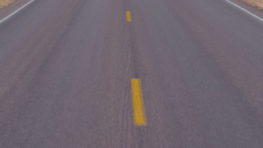 AERIAL: Flying above the empty road leading past the dry grasslands prairie into the amazing Badlands landscape with rocky sandstone mountains. Traveling across the dry Badlands desert in South Dakota
