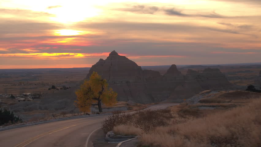 Amazing sunset sky behind the rocky sandstone formations in Badlands National Park. Winding road through Badlands grassland desert in South Dakota at reddish sunrise. Road trip across United States