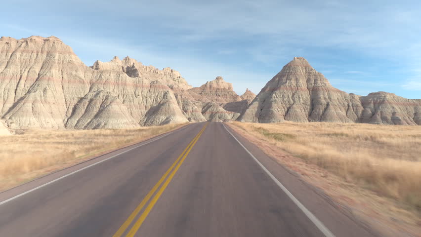 FPV: Driving along the empty road winding past amazing Badlands landscape with rocky sandstone mountains. Traveling across the Badlands grassland desert in South Dakota. Road trip across United States