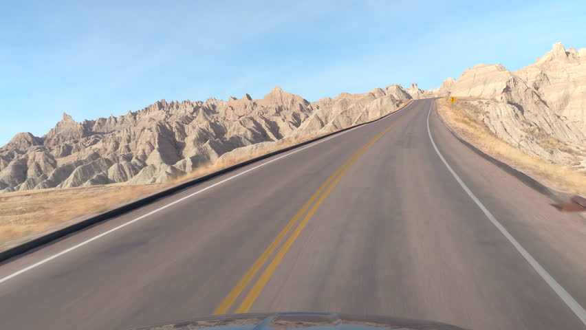 FPV: Driving along the empty road winding into amazing Badlands landscape with rocky sandstone mountains. Traveling across the Badlands grassland desert in South Dakota. Road trip across United States