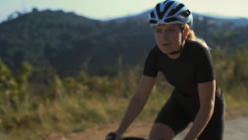 Close up soft focused shot of female athlete cyclist climbing dramatically up the difficult climb breathes deeply as the excersize gets harder, training plan to reach her goals for healthy lifestyle Royalty-Free Stock Footage #27682726