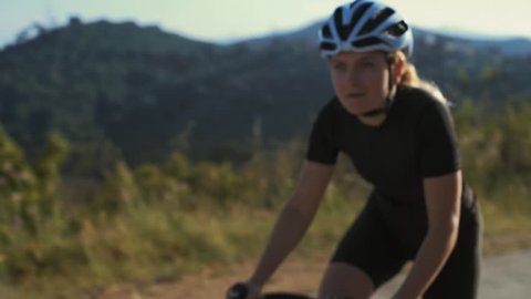 Close up soft focused shot of female athlete cyclist climbing dramatically up the difficult climb breathes deeply as the excersize gets harder, training plan to reach her goals for healthy lifestyle