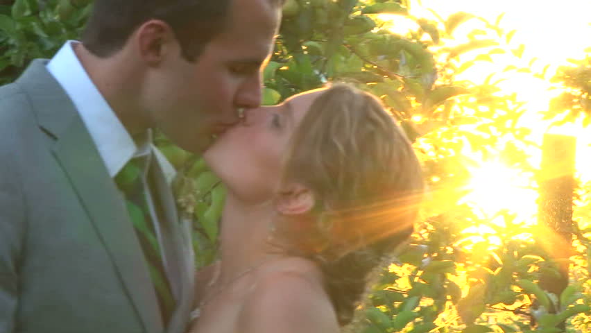 Model releases bride and groom kissing at sunset on their wedding day.