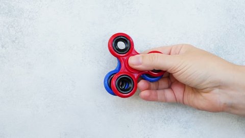 someones hand showing trick with two fidget spinners on light gray background, popular relaxing toy, generic design