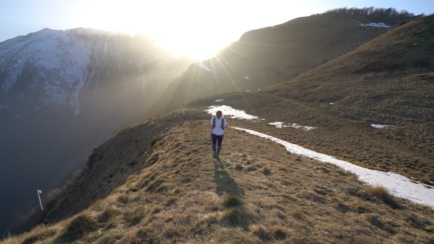 Trekking young woman hiking on hike with backpack, healthy active lifestyle. Hiker female walking away on hike in beautiful mountain nature landscape in the Swiss alps, Switzerland.