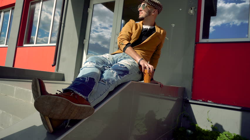 glamorous fashion guy in the CAP and glasses sitting on the stairs