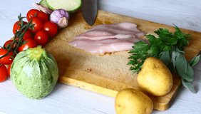 Chef chopping chicken breast on wooden cutting board with near mixed vegetable 