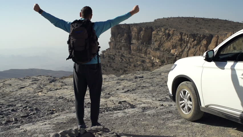 Successful man with backpack raising arms in victory near canyon, super slow motion 240fps
