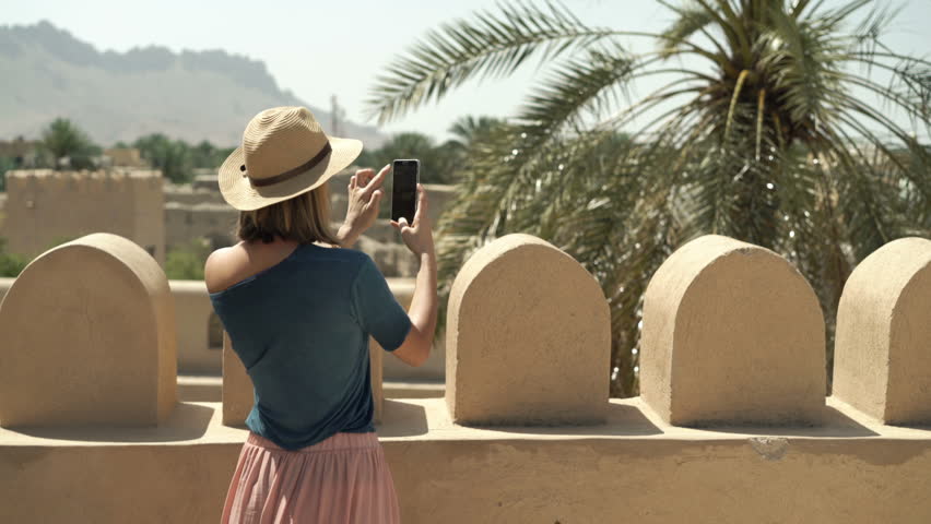 Woman taking photo with cellphone of ancient fort in Oman

