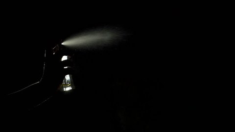 Close-up silhouette of a girl spraying perfume in the dark, slow motion.