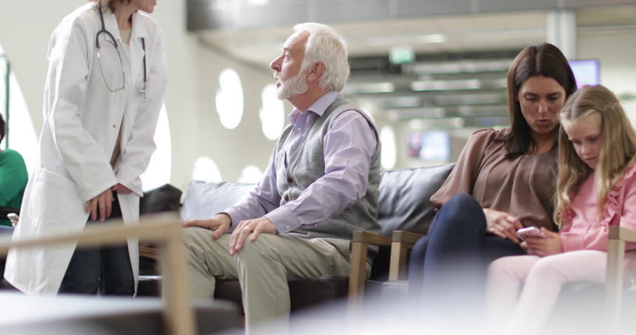 Senior Male talking to Doctor in a crowded hospital waiting room
