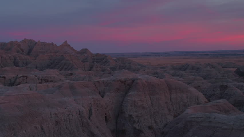 AERIAL: Beautiful reddish sky above sandstone mountaintops in Badlands National Park at sunset. Stunning sunrise above eroded rocky mountain formations in S Dakota, United States