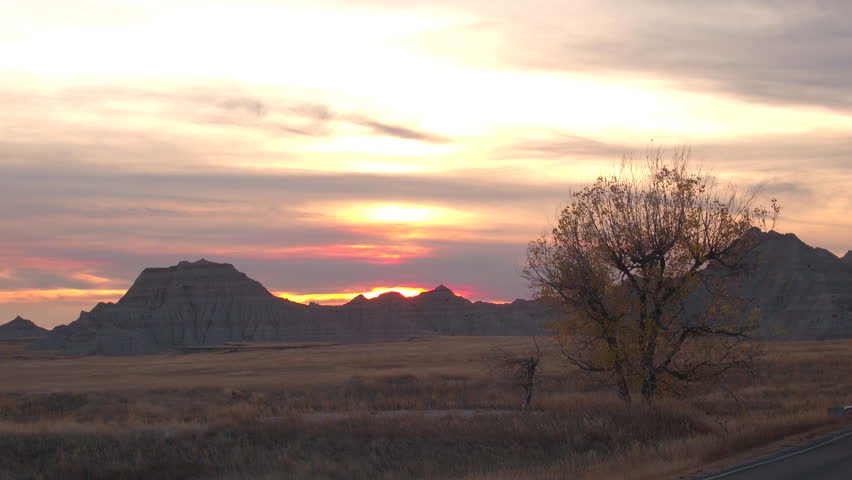 AERIAL Beautiful endless sandstone formations and dry grass prairie at Badlands National Park at sunset. Stunning landscape with eroded rocky mountains rising out of vast grasslands at reddish sunrise