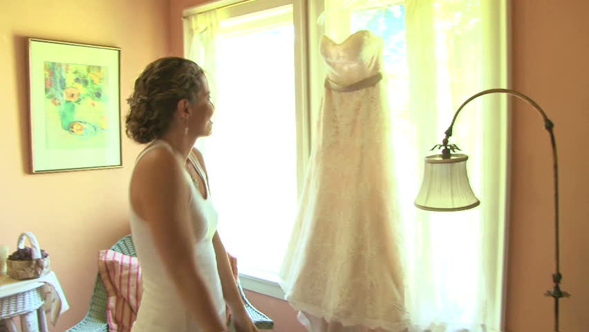 Model released bride hanging up her wedding dress and smiling on her wedding