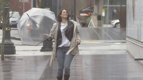 Young beautiful Latin woman dancing around with an umbrella in the city while listening to music