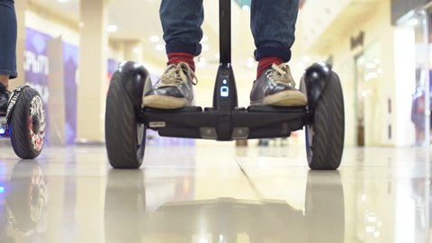 Teenager on hyroscooter in a modern shopping center. Close up of man's legs on two wheels electric gyro scooter