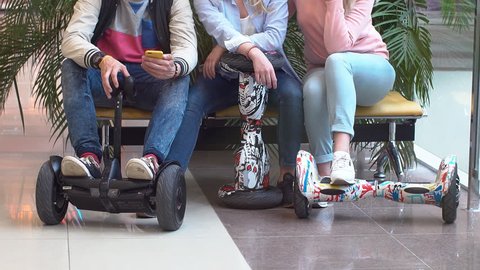 A group of teenagers with hyroscooter in the mall. The guy uses a mobile phone in the company of friends