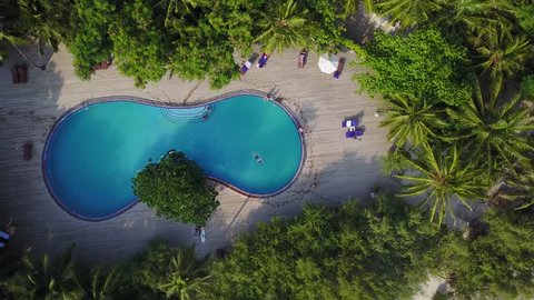 Maldives island, camera is rising over the swimming pool on luxury hotel. Aerial video of resort with lots of palms, bungalows, beach and indian ocean. 