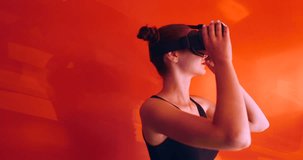 Excited Caucasian female in casual clothes using VR headset indoors, watching 360. Red wall background. 4K UHD RAW edited footage 