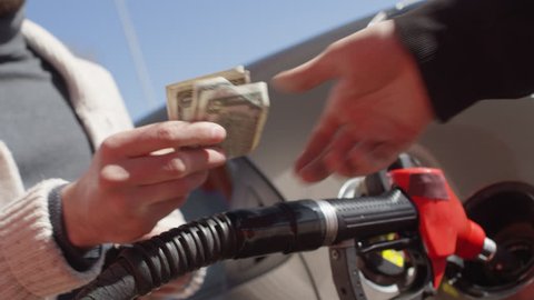 Low angle view of young man taking off cash from wallet and paying to gas station attendant for filling up car. Slow motion shot