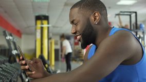 Successful smiling athlete scrolling photos on smartphone at fitness club