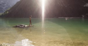 Young active man running and diving into wild sunny clear lake.Group of friends summer adventure journey in mountain nature outdoors.Travel exploring Alps,Dolomites,Italy.4k slow motion 60p