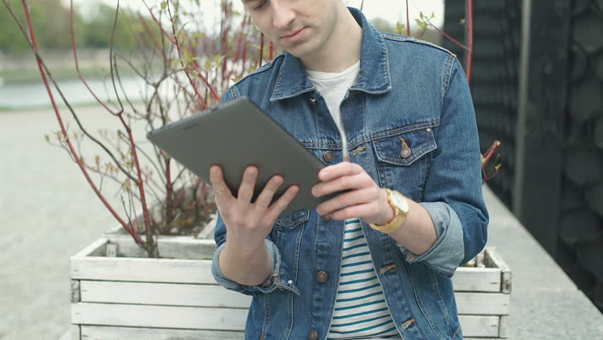 Stylish man browsing internet on tablet and smiling to the camera, steadycam shot
