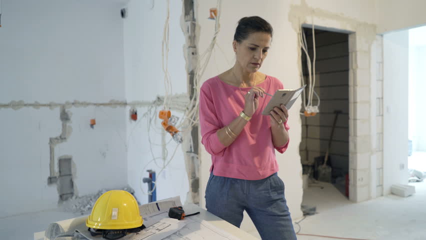 Young woman texting on smartphone standing at new home
