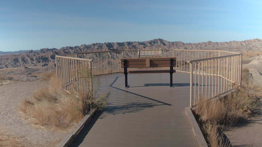 CLOSE UP: Empty bench with a view of sunny Badlands National park on a sunny day. Lonely bench at the end of a boardwalk overlooking stunning desert landscape and high pointy mountains in South Dakota