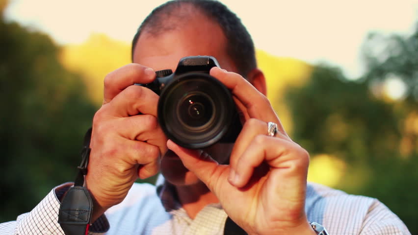 A smiling photographer frames-up a shot to camera.