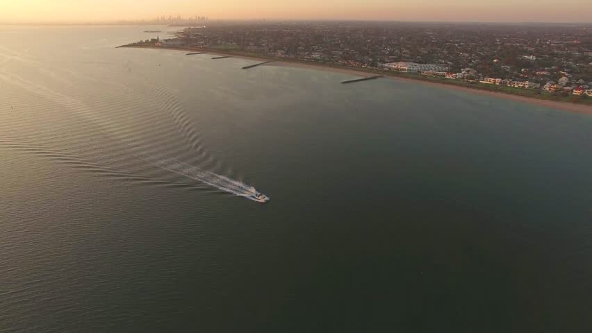 Static aerial view of boat sailing along Melbourne coastline at sunset