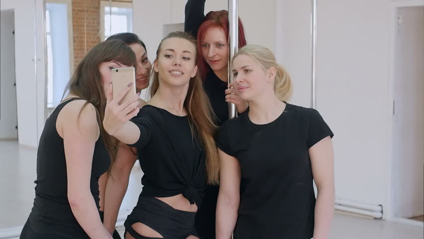 Group of beautiful young women taking a selfie with smartphone during a pole dance class